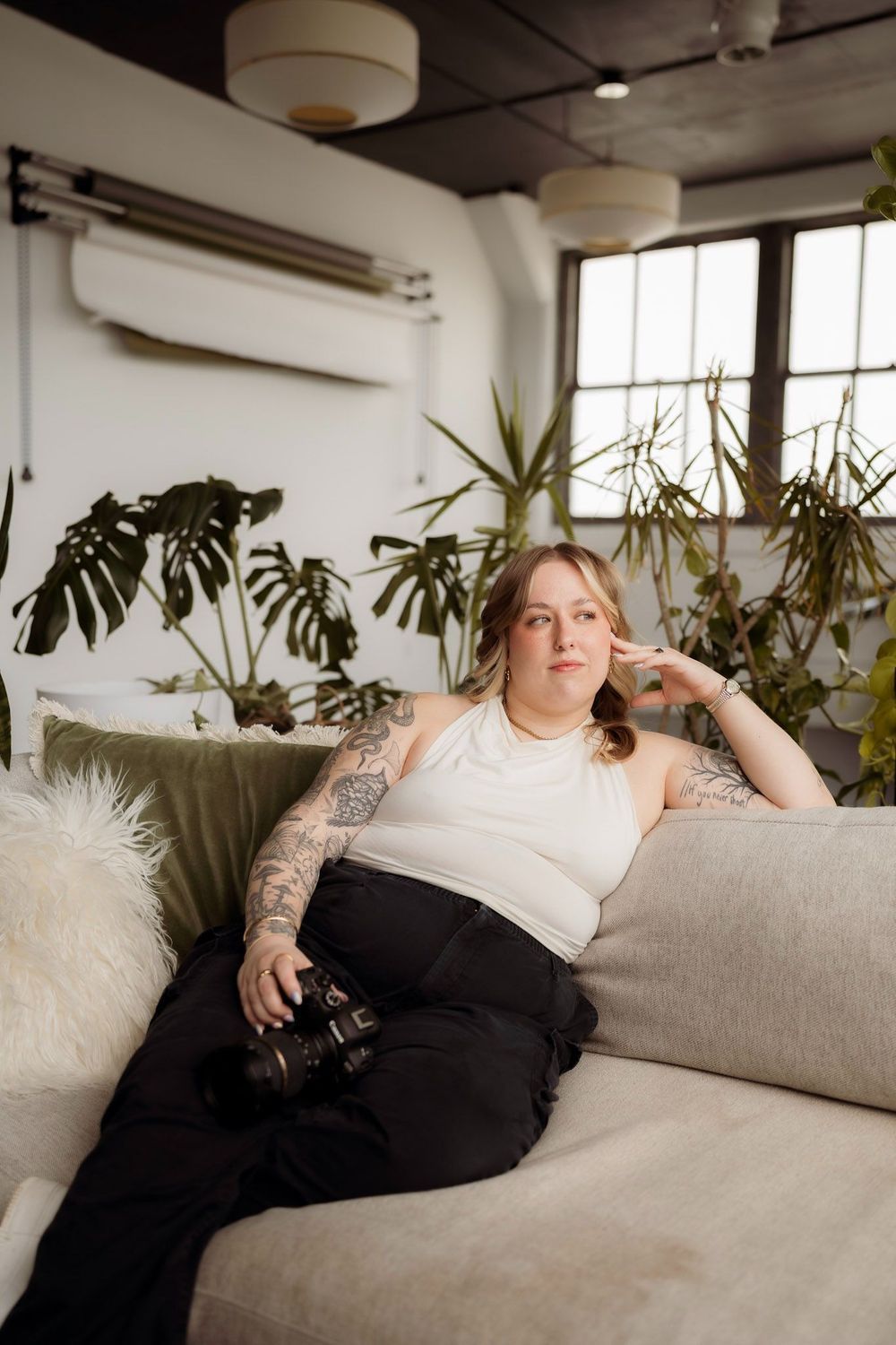 Liv Finley relaxing on a couch holding her camera, surrounded by plants in a bright studio space