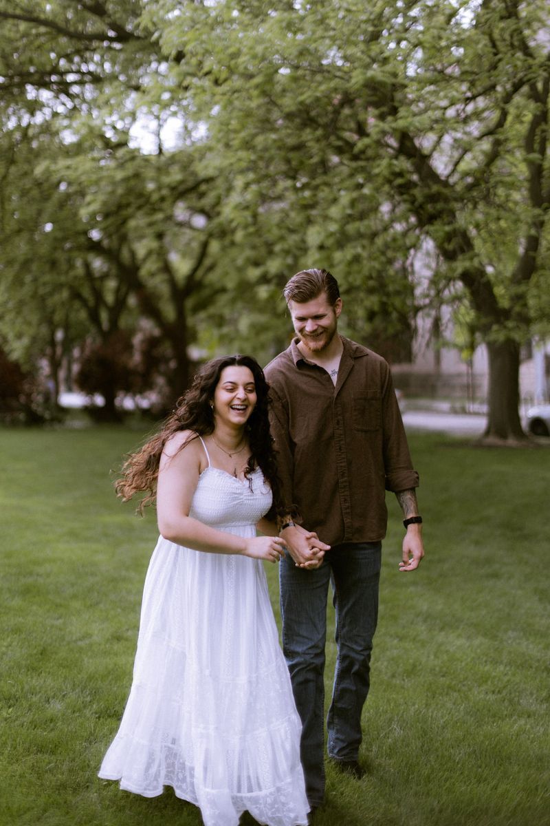 Couple laughing and holding hands while walking through a lush green park