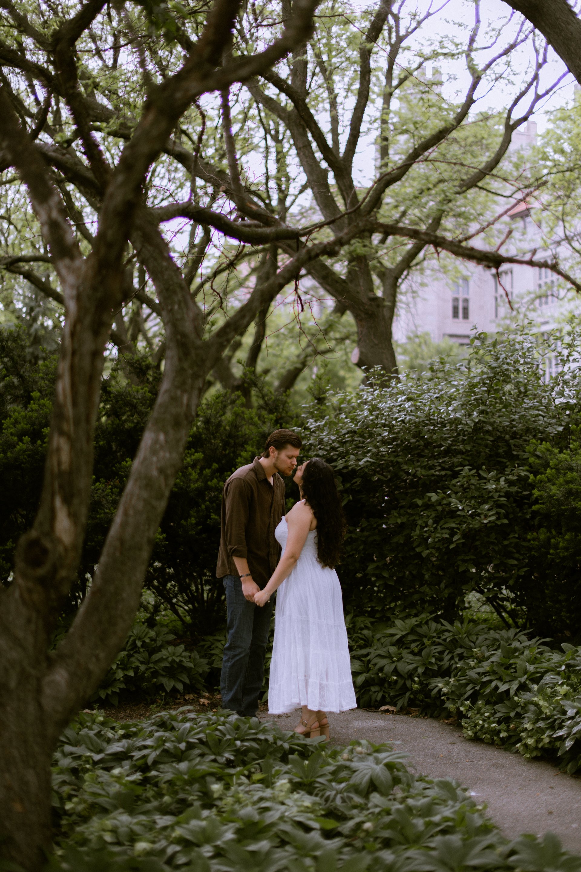 Couple sharing a close moment on a garden path, framed by arching trees and lush greenery
