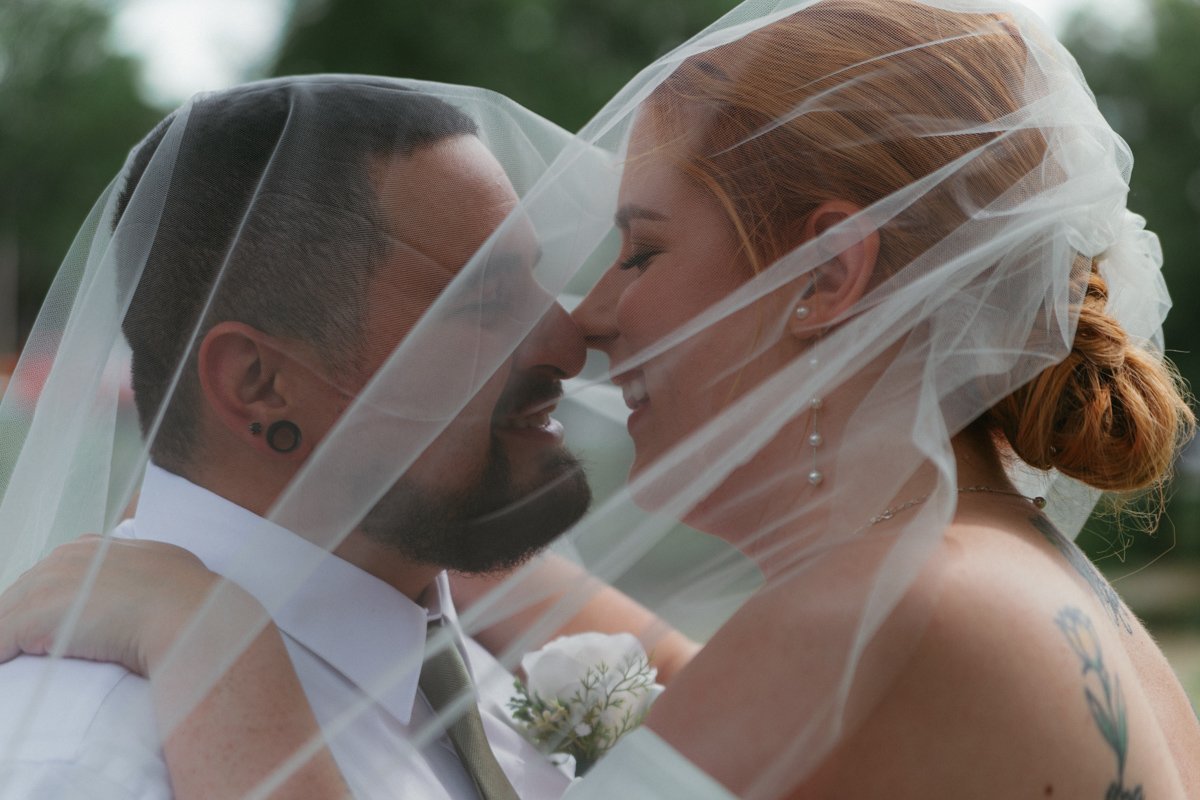 Bride and groom smiling face to face under a flowing veil, almost kissing